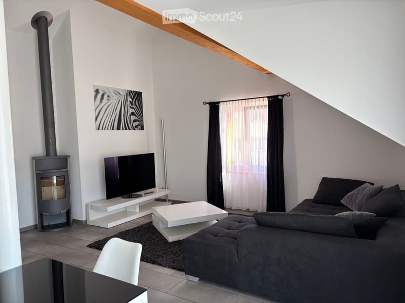 Modern living room with a dark grey sectional sofa, white coffee table, flat-screen TV on a white stand, fireplace, and large window with curtains.