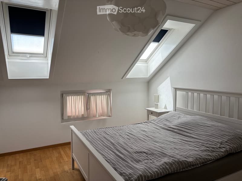 Bright, modern bedroom with wooden flooring, large windows, skylights, and a neatly made bed with striped bedding.