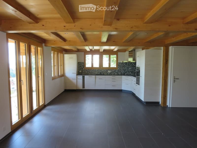 Modern kitchen with white cabinets, dark tiled floor, and exposed wooden beams on the ceiling. Features a central island with sink and oven, and large windows with wooden frames.