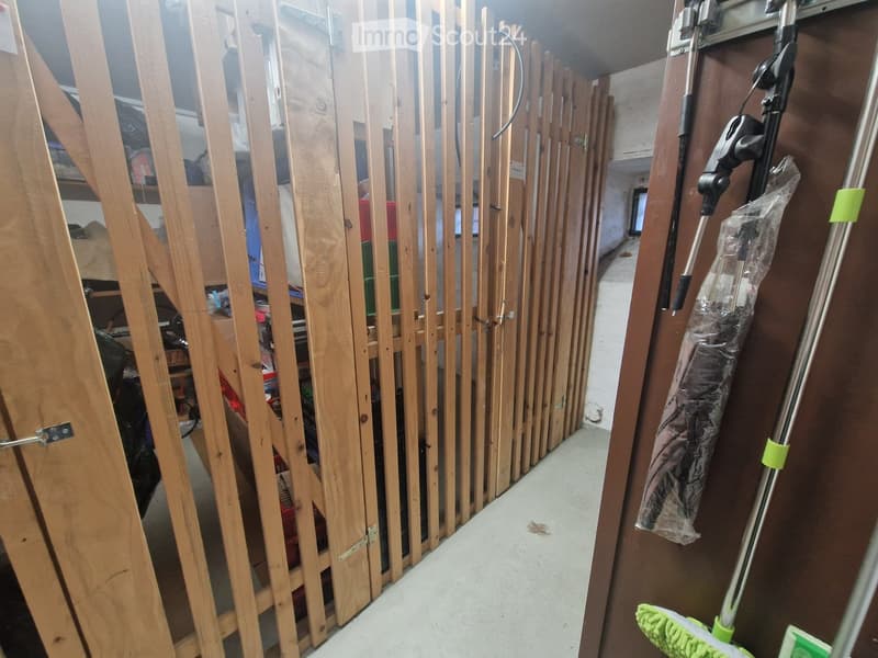 A narrow hallway with unfinished wooden paneling on one side and a storage area on the other, featuring a vacuum cleaner and cleaning supplies.