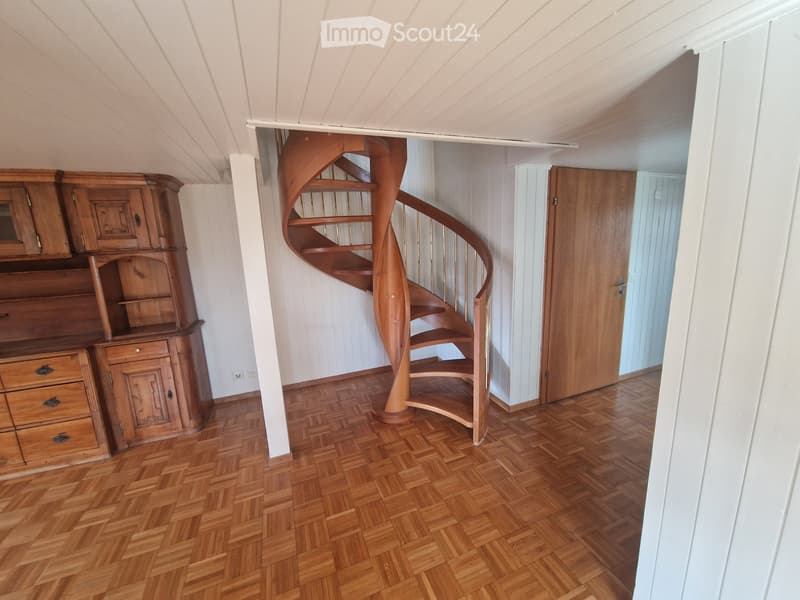 Spacious room with wooden parquet flooring, a wooden cabinet, and a spiral staircase leading upwards.