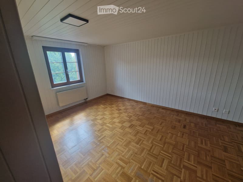 Empty room with wooden herringbone flooring, white paneled walls, a single window with white frame, and a radiator below it. The ceiling has a recessed light fixture.