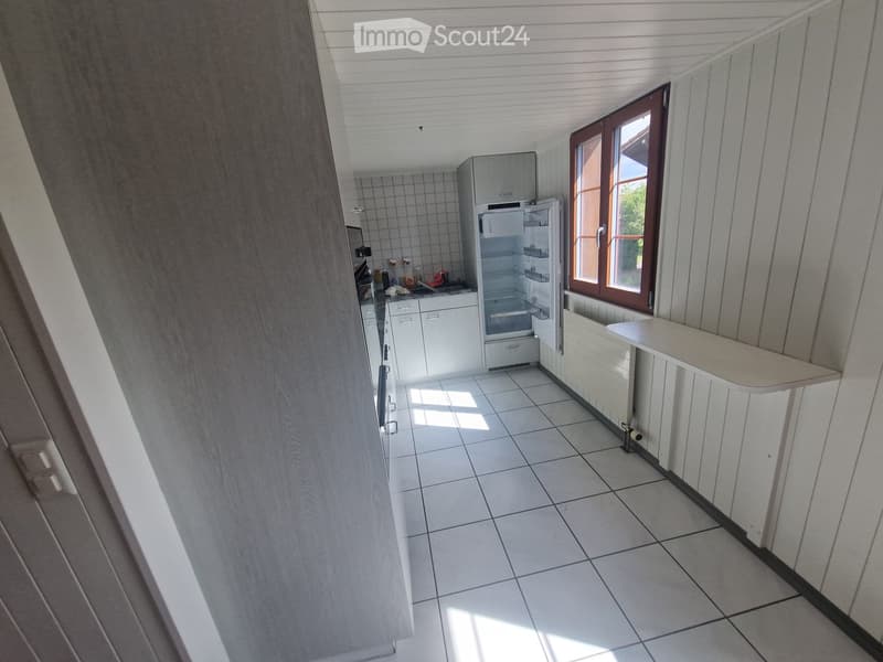 Modern kitchen with white tiled floor, white cabinets, and a stainless steel refrigerator. Features a window with wooden frame and a countertop.