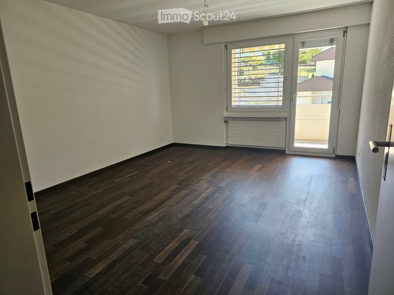 Empty room with wooden flooring, white walls, and a large sliding glass door leading to a balcony.