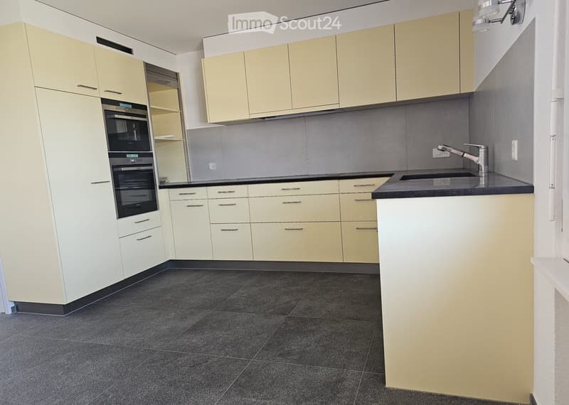 Modern kitchen with light-colored cabinets, dark countertops, and a built-in oven. Features a sink with a modern faucet and a dark tiled floor.