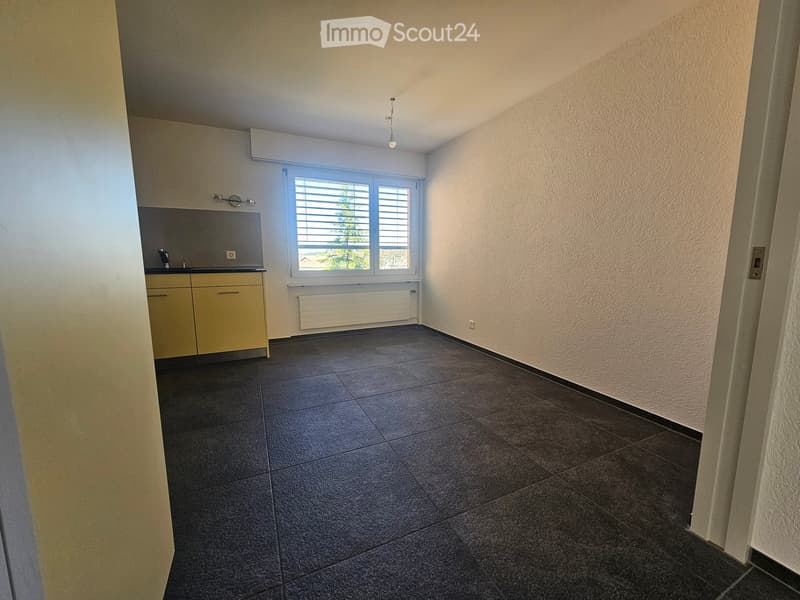 Empty kitchen with tiled floor, light-colored cabinets, a window with blinds, and a radiator below the window.