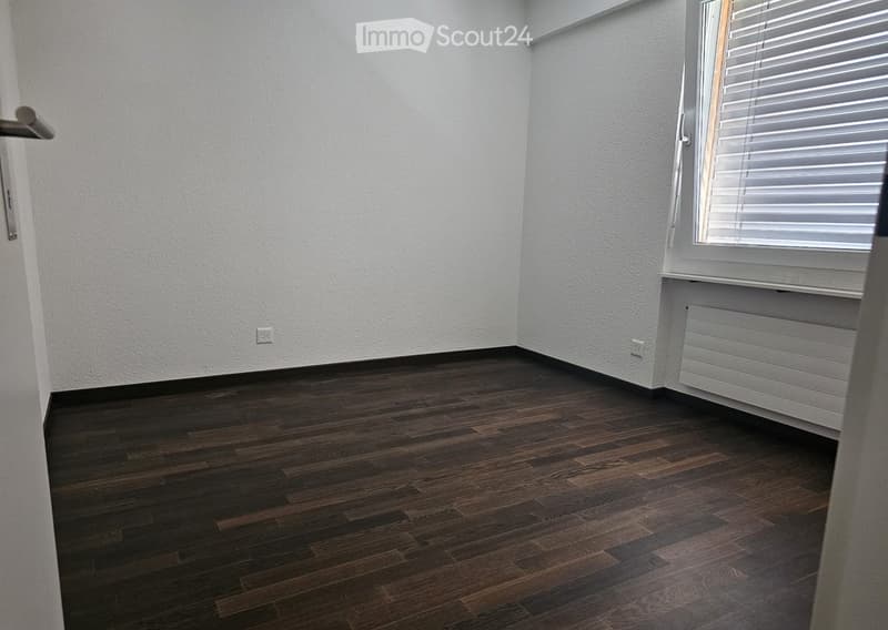Empty room with dark wooden flooring, white walls, and a window with blinds. No furniture or equipment is present.