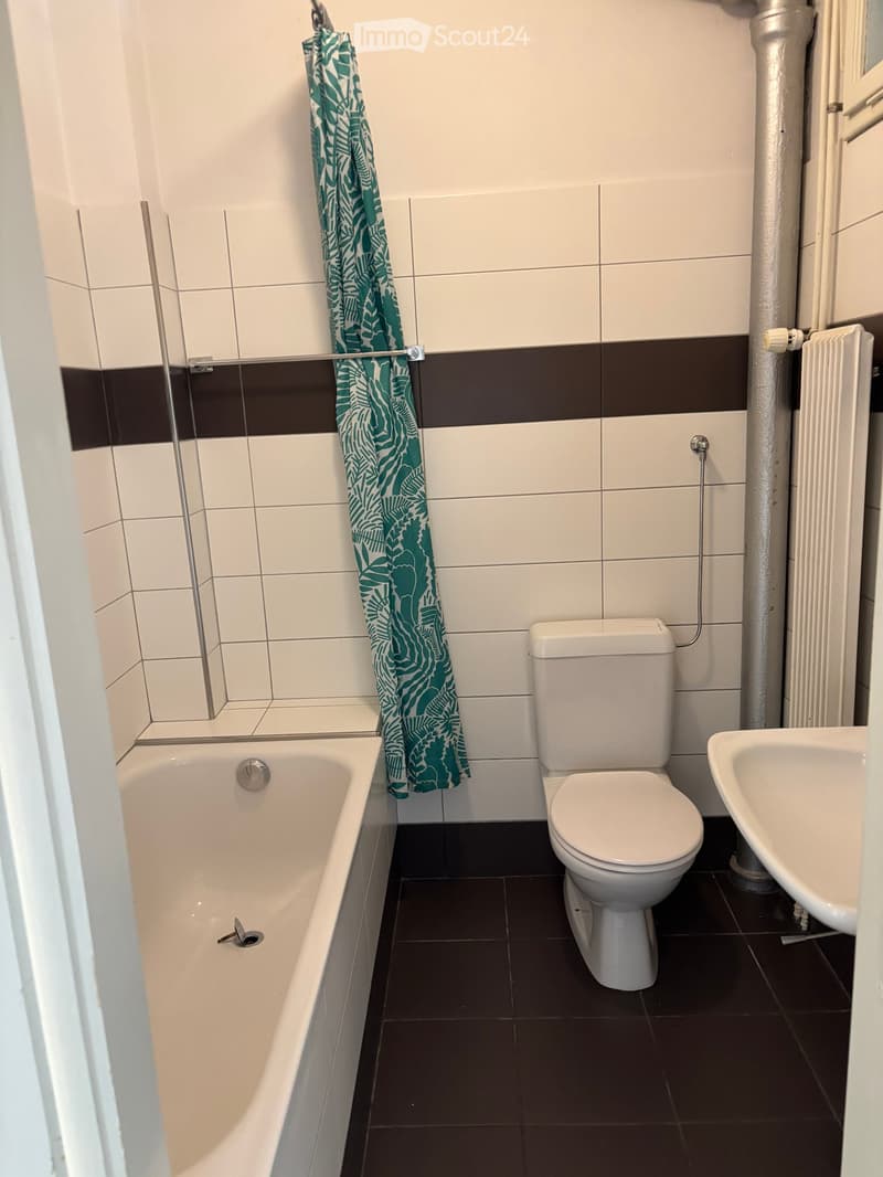 Bathroom with white tiles, dark floor, bathtub, toilet, sink, and a green shower curtain.