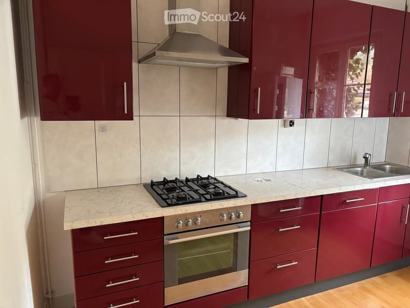 Modern kitchen with red cabinets, marble countertops, gas stove, oven, and stainless steel sink.