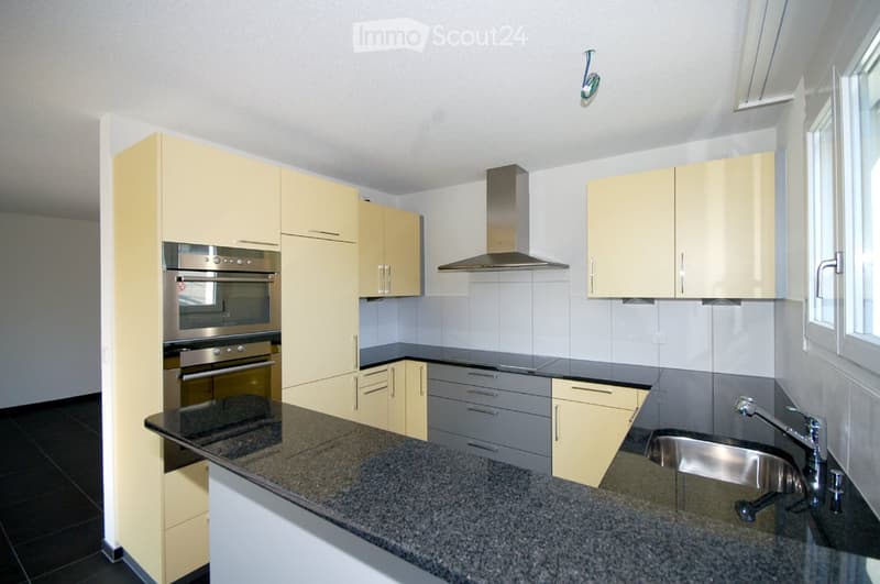 Modern kitchen with light yellow cabinets, stainless steel appliances, granite countertop, and a sink with a modern faucet.