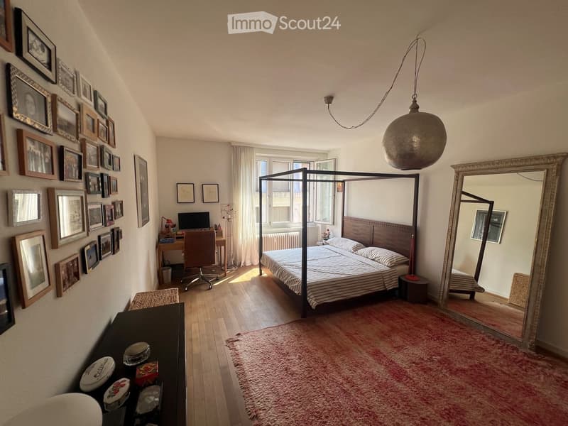 Cozy bedroom with a four-poster bed, wooden floor, large mirror, desk with chair, and wall adorned with framed pictures.