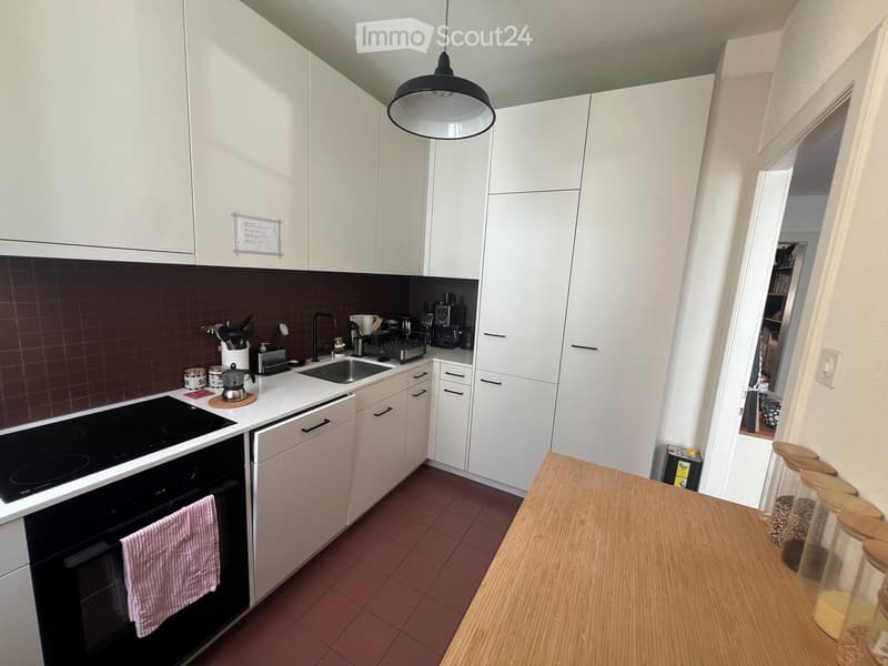 Modern kitchen with white cabinets, dark backsplash, and stainless steel appliances. Features an electric stovetop, oven, sink, and coffee maker on the counter.