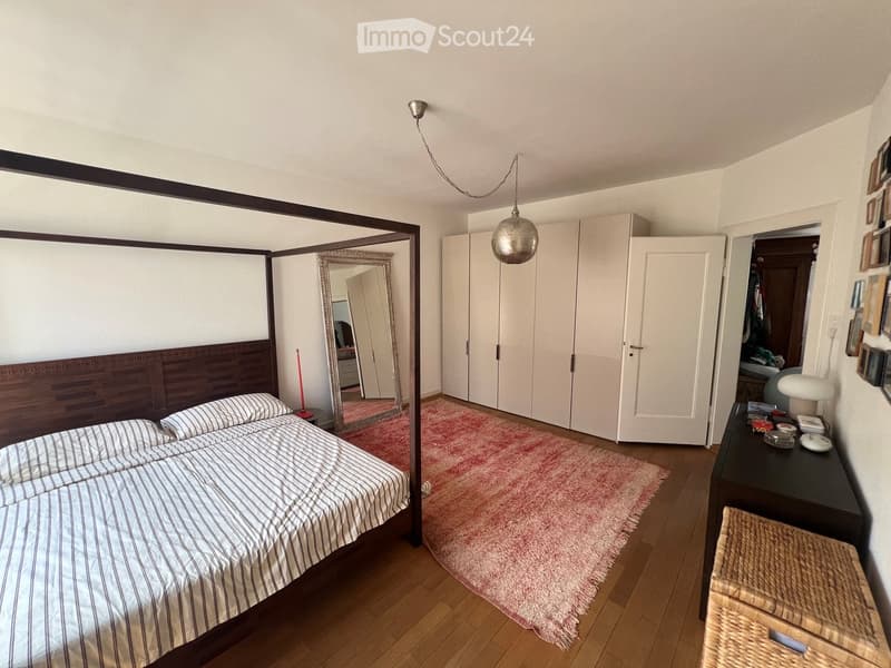 Modern bedroom with a four-poster bed, striped bedding, a pink shag rug, a large mirror, and a nightstand with a lamp.