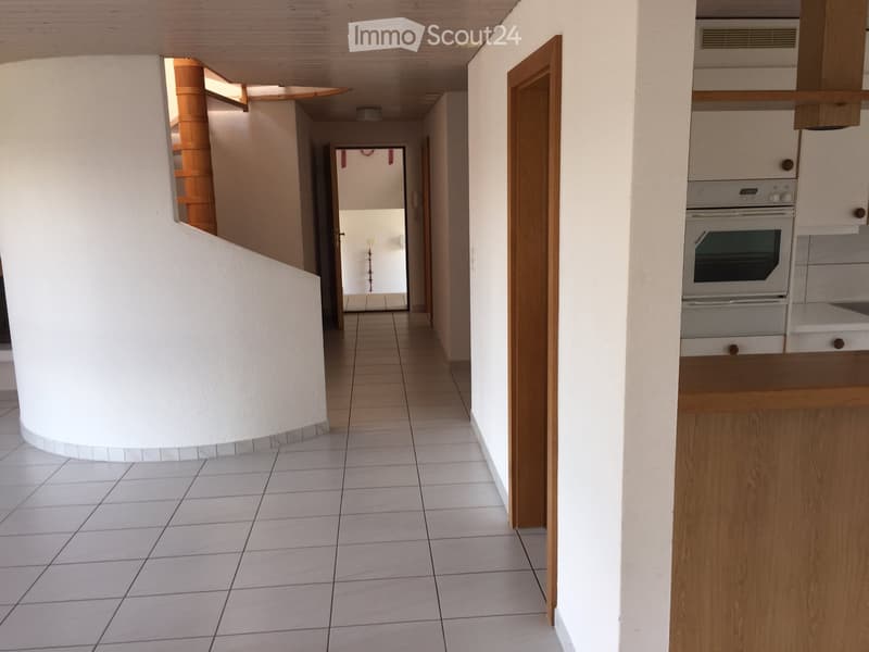 Empty hallway with white tiles, wooden doors, spiral staircase, kitchen with oven and cabinets