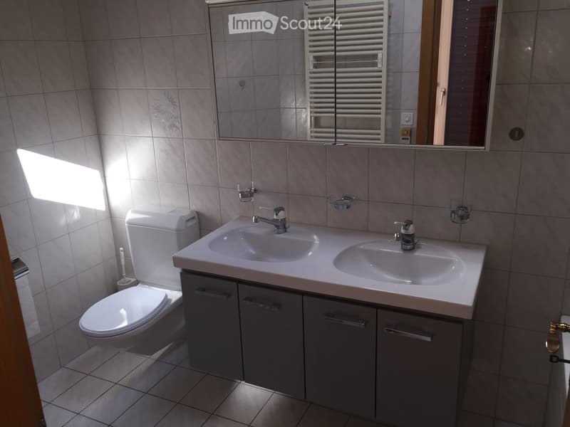 Bathroom with white tiles, double sink, mirror, toilet, and cabinets