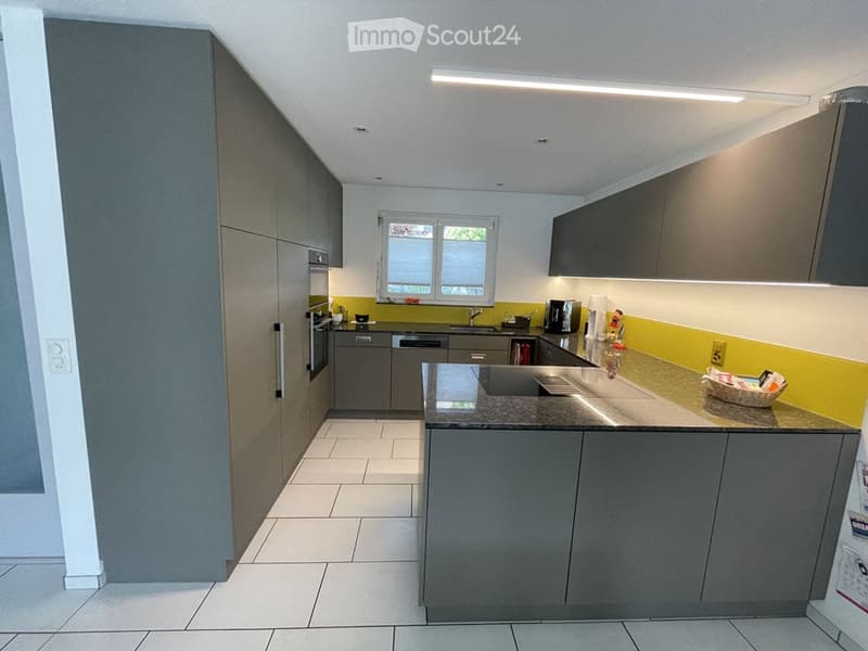 Modern kitchen with grey cabinets, white tiled floor, and a central island with a countertop. Features include a sink, oven, dishwasher, and coffee maker.