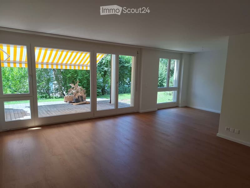 Empty room with wooden flooring, large windows, and sliding glass doors leading to a patio area.