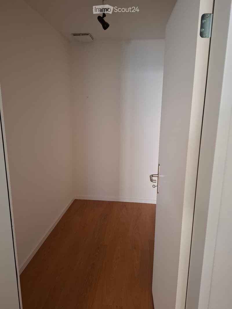 Empty hallway with light wooden flooring and white walls, featuring a partially open door on the right side.