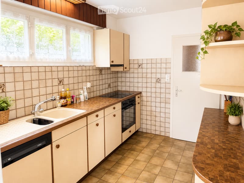 A well-lit kitchen with light-colored cabinets, a wooden countertop, a sink with a faucet, an oven, and a dishwasher. The backsplash is tiled, and there are potted plants on the counters.