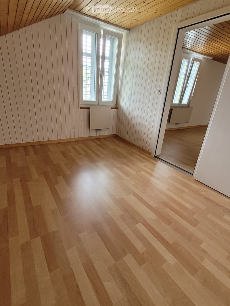 Room with wooden floors, white walls, white-framed windows, and two radiators below the windows.