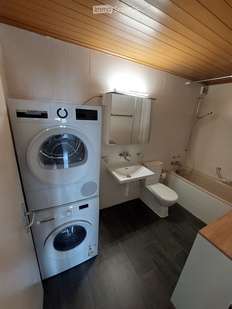 Washer on top of dryer, white bathroom with bathtub, sink, toilet, tiled floor