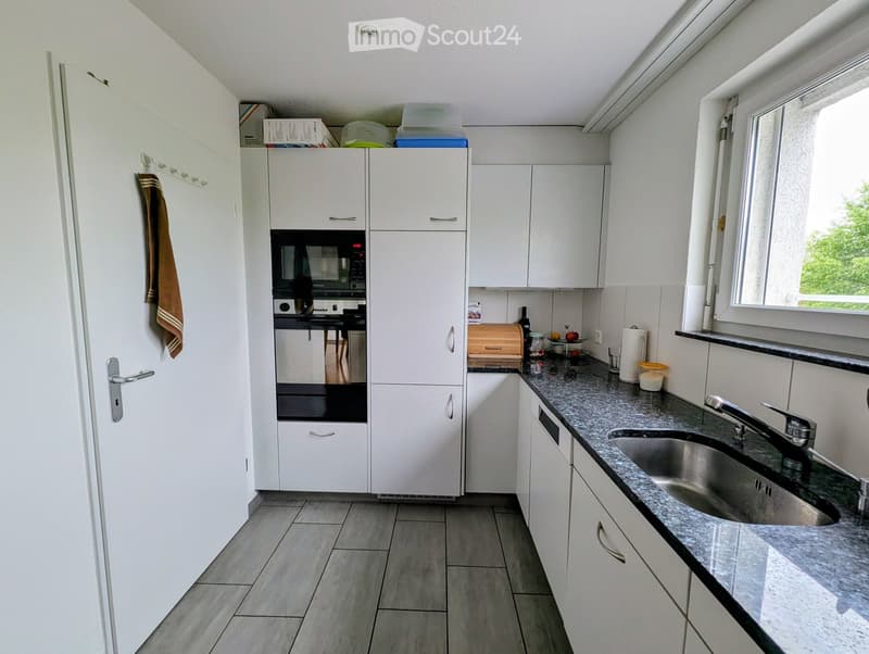 Modern kitchen with white cabinets, granite countertop, stainless steel sink, and various appliances including an oven and microwave. A towel hangs on the door.