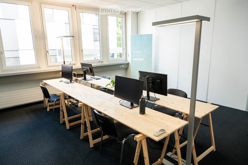 Modern office space with wooden tables, black chairs, multiple computer screens, and a water bottle on the table.