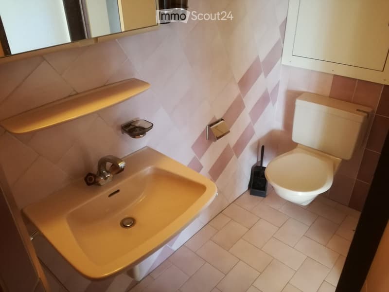 Bathroom with a sink, toilet, mirror, and tiled walls and floor.