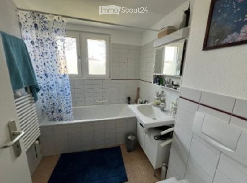 Bathroom with a bathtub, sink, mirror, shower curtain, and a towel on the floor.