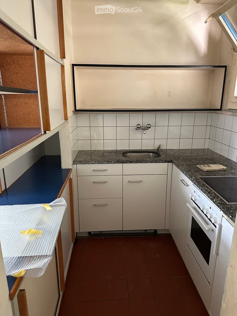 Compact kitchen with white cabinets, granite countertops, a sink, and an oven. The space is clean and organized, with a small window providing natural light.