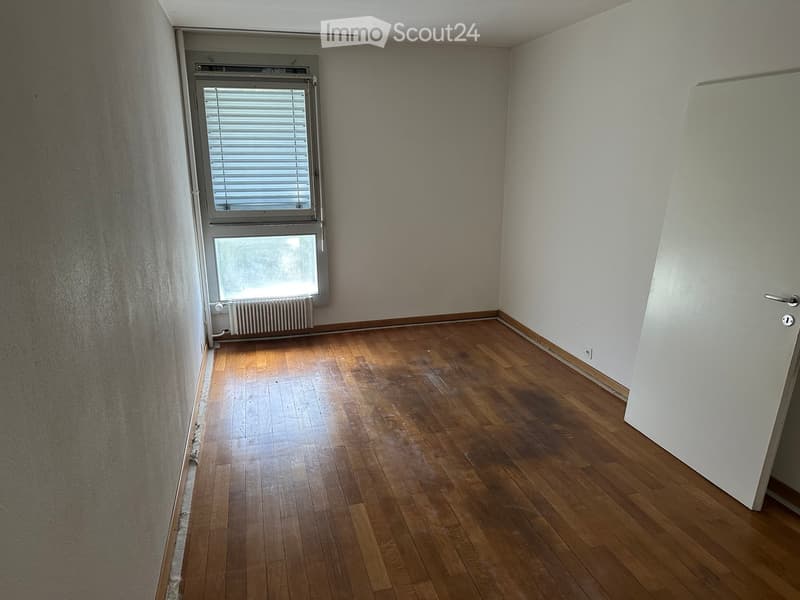 Empty room with wooden flooring, white walls, and a window with blinds. A radiator is visible below the window.