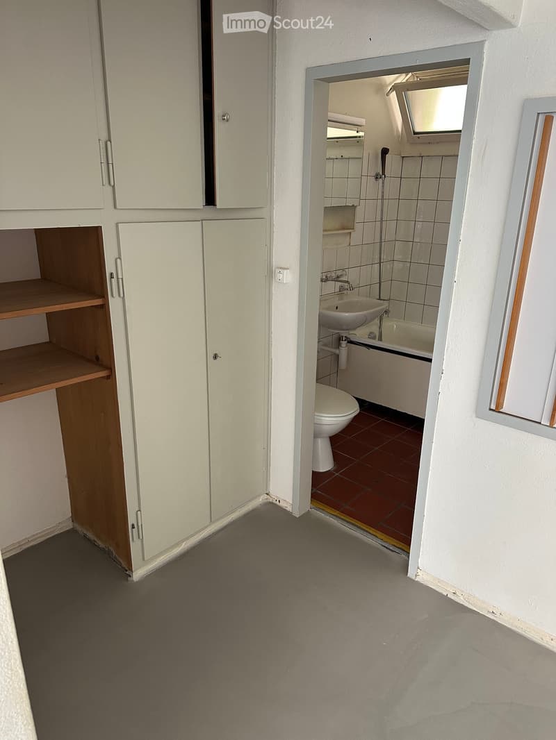 Bathroom with a toilet, sink, bathtub, and white cabinets. The floor is tiled in red, and the walls are white.