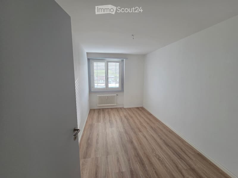 Empty room with light wooden flooring, white walls, a window with blinds, and a radiator below the window.