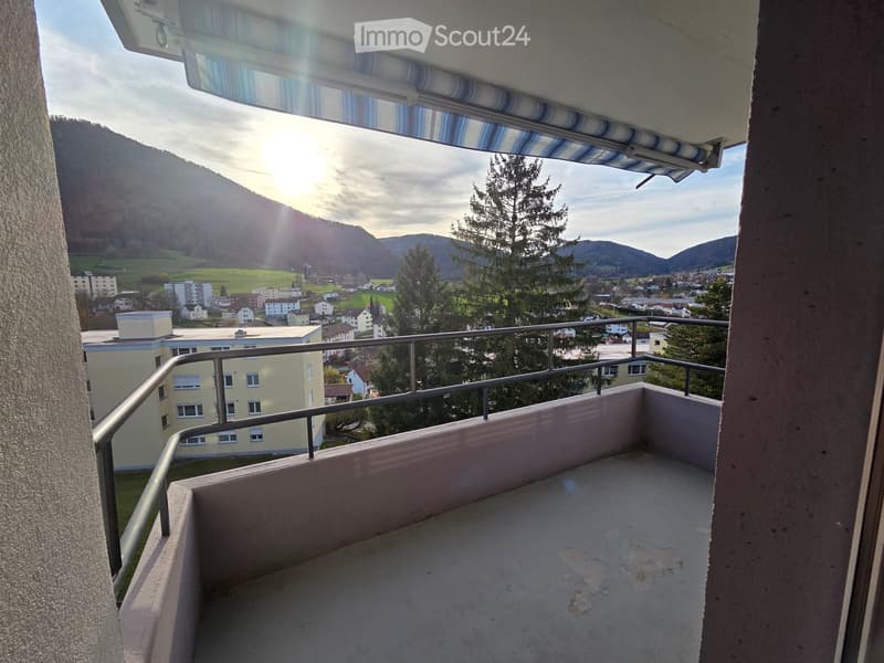 Balcony with metal railing, overlooking a town and mountains, with a retractable awning and a view of the landscape.
