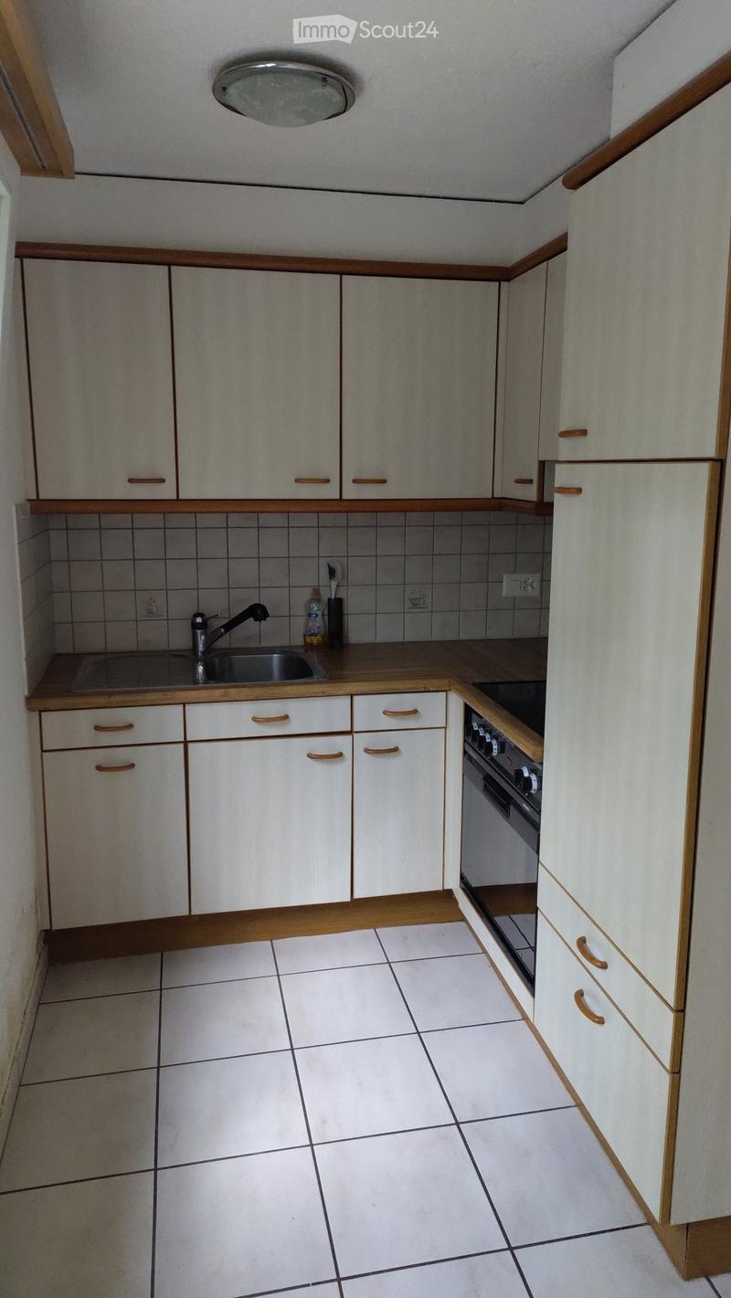 Kitchen. A small, unfurnished kitchen with white cabinets, wooden countertops, and tiled flooring. The sink and oven are visible, along with a few cleaning supplies on the counter.