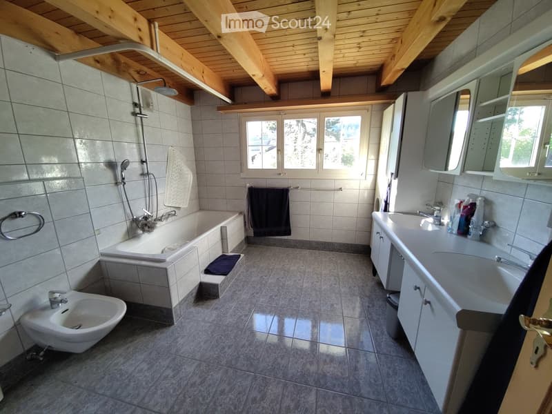 Bathroom. Bathroom with a bathtub, sink, mirror, and bidet. Features tiled walls and floor, wooden ceiling beams, and a window with a view of greenery.