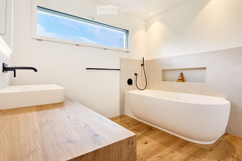 Modern bathroom with a large window, white bathtub, sink, and wooden floor.