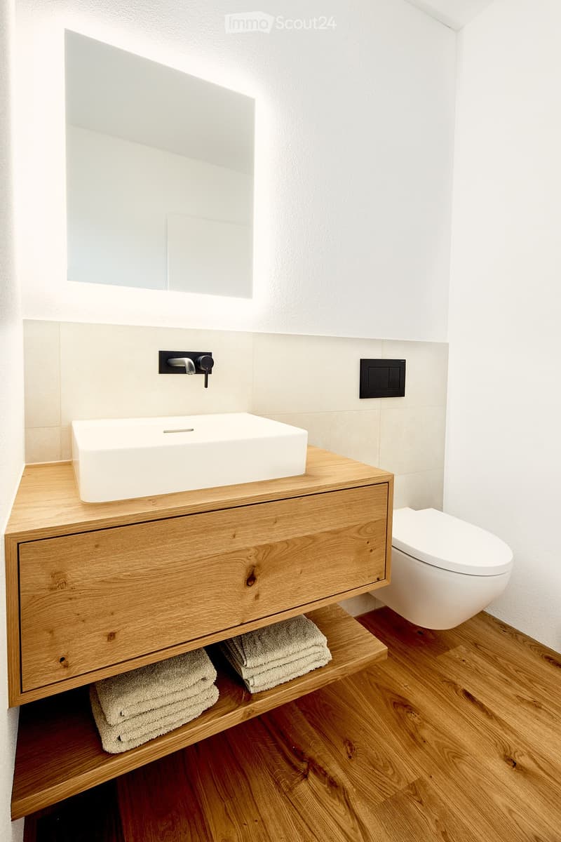 Modern bathroom with a wooden vanity, white sink, mirror, and neatly folded towels underneath.
