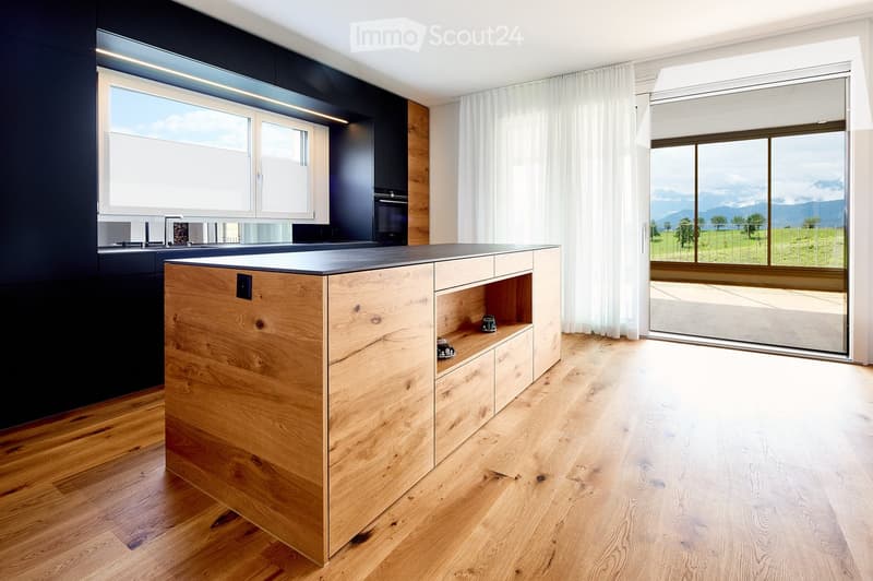 Modern kitchen with a wooden island, sleek black cabinets, and large windows offering a scenic mountain view.