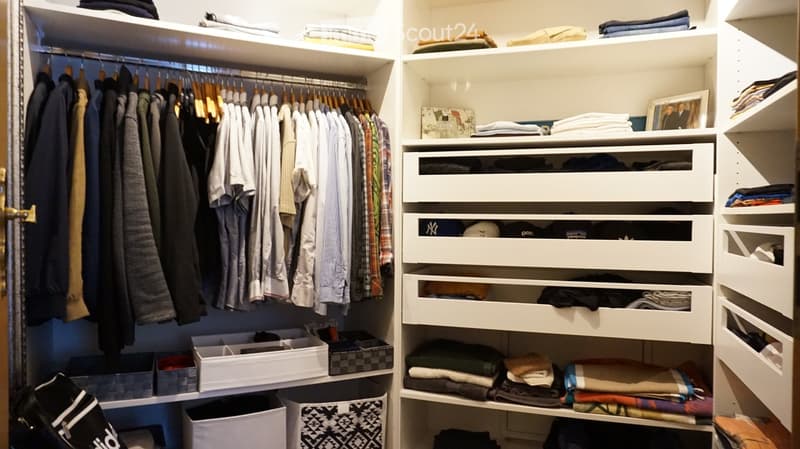 A well-organized walk-in closet with white built-in wardrobes, multiple drawers, shelves, and neatly arranged clothing and accessories.