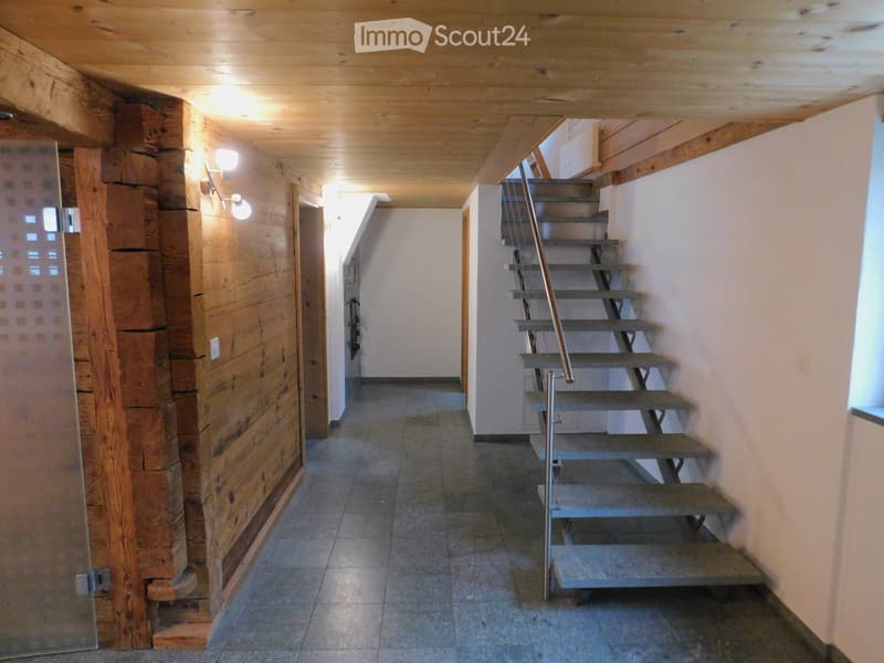 Wooden-paneled hallway with a staircase leading upwards, featuring a metal handrail and wooden steps.