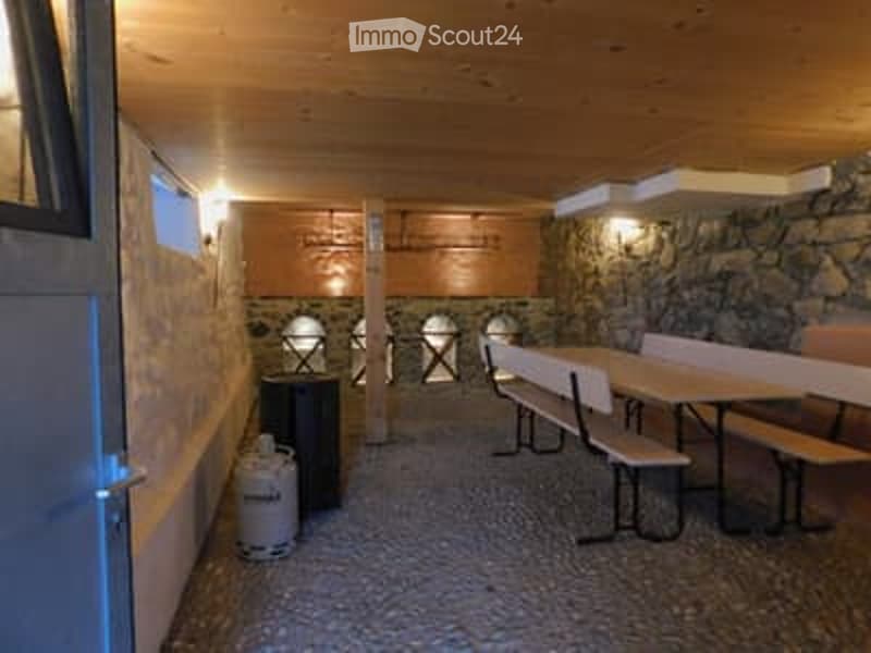 A rustic, wooden-paneled room with stone walls, featuring benches, tables, and a cabinet. The space has warm lighting and a cozy, traditional design.