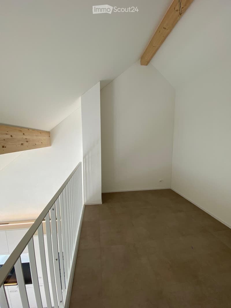 Empty hallway with white walls, beige tiled floor, and a metal railing leading to another level.