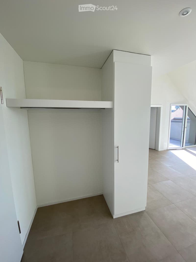 Empty room with white walls, tiled floor, built-in closet with mirrored doors, and a sliding glass door leading outside.