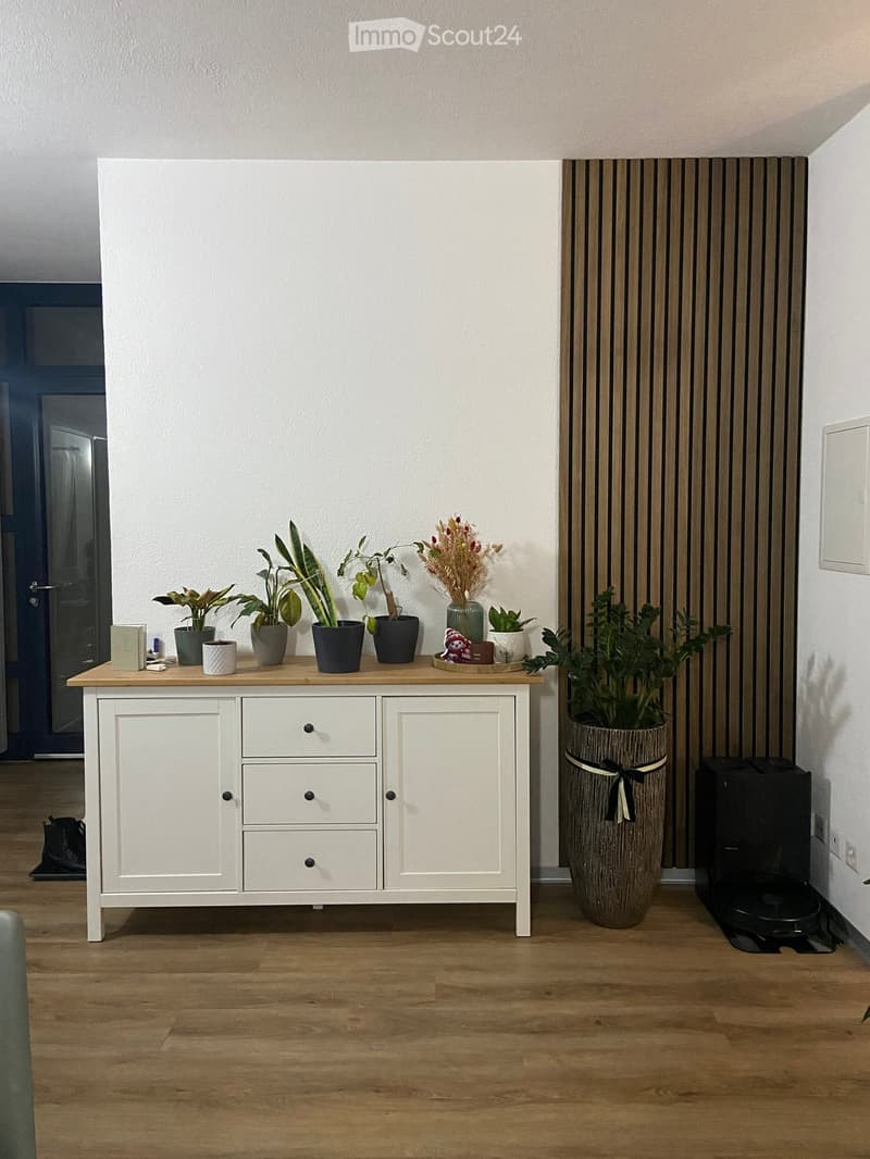 A modern hallway with a white cabinet, wooden table, and various decorative items including plants and vases.