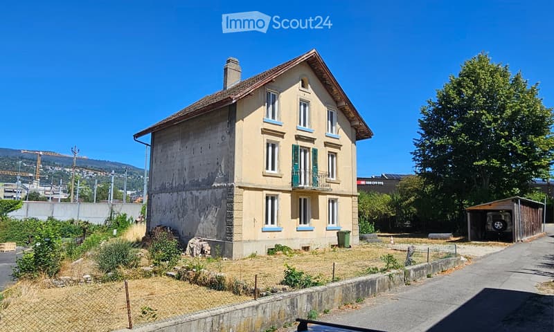 Two-story house with a pitched roof, multiple windows, and a small balcony. The building has a mix of stone and plaster exterior, with a visible chimney and a small garage to the right.