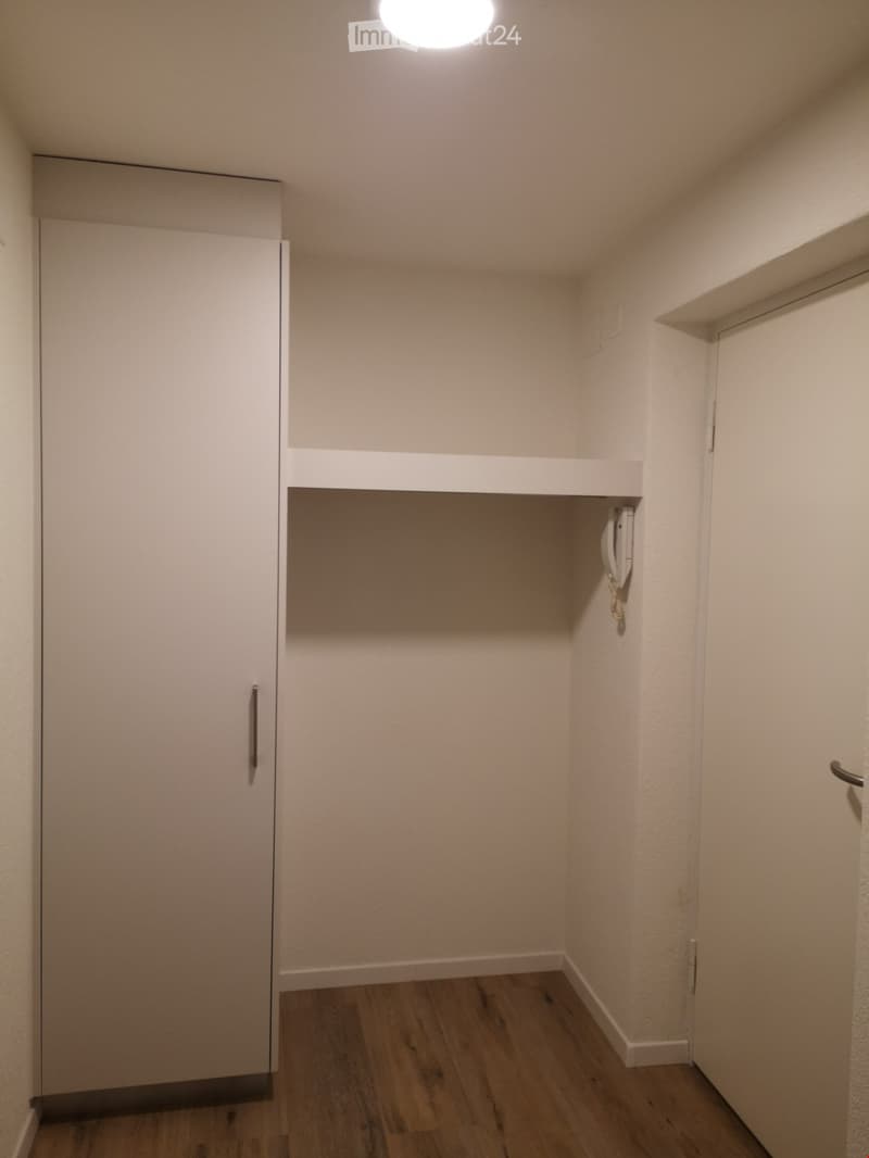 Empty hallway with wooden flooring, white walls, and a closed door on the left side.