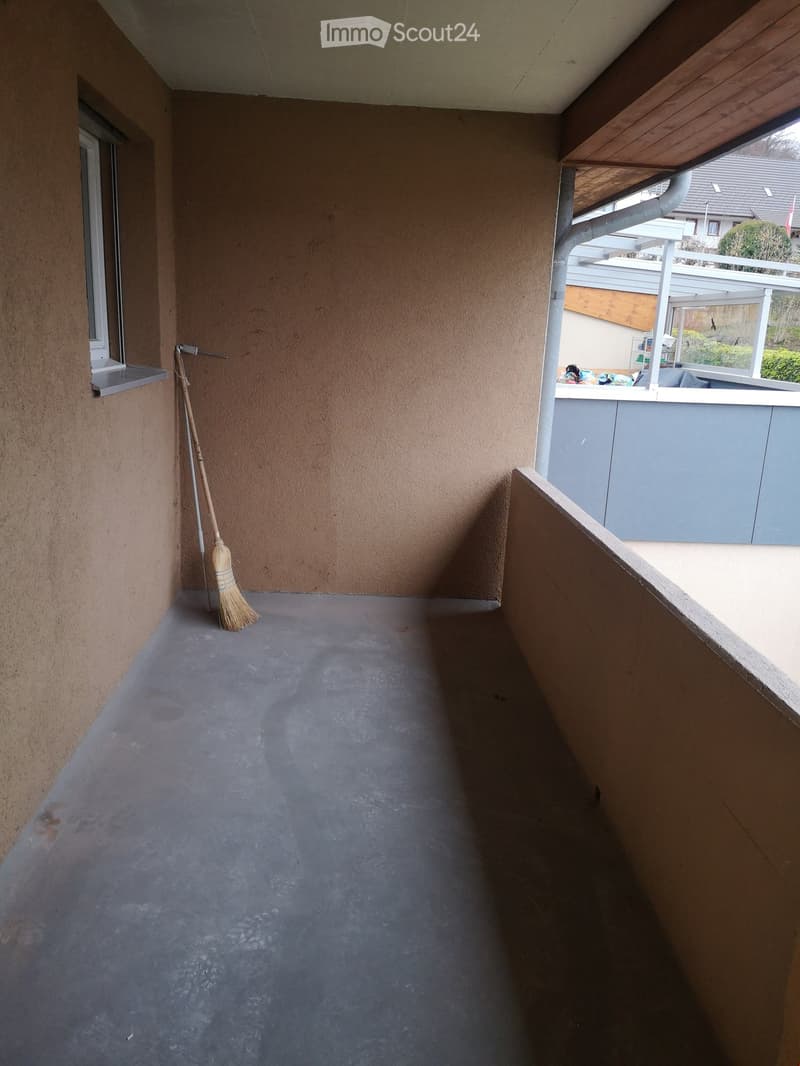 Empty balcony with concrete floor, wooden railing, and a broom leaning against the wall.