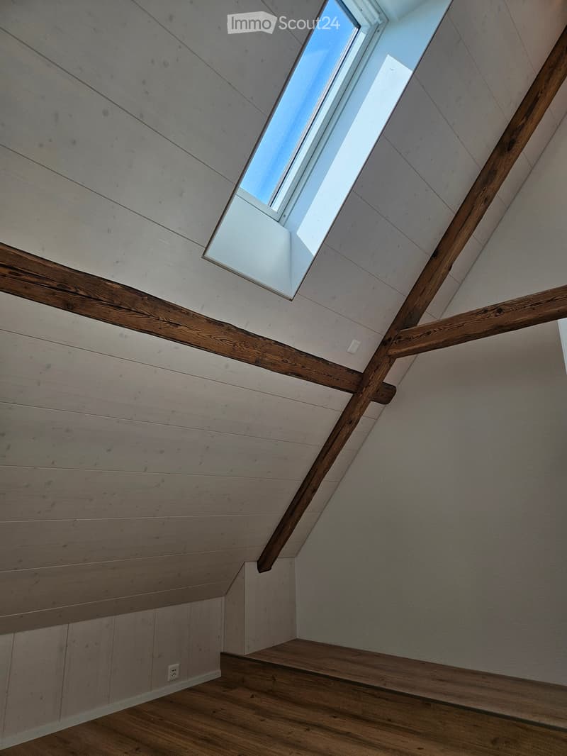 Wooden staircase with slanted ceiling and skylight window, light wood paneling on walls and ceiling, wooden handrails, and a small electrical outlet visible on the wall.