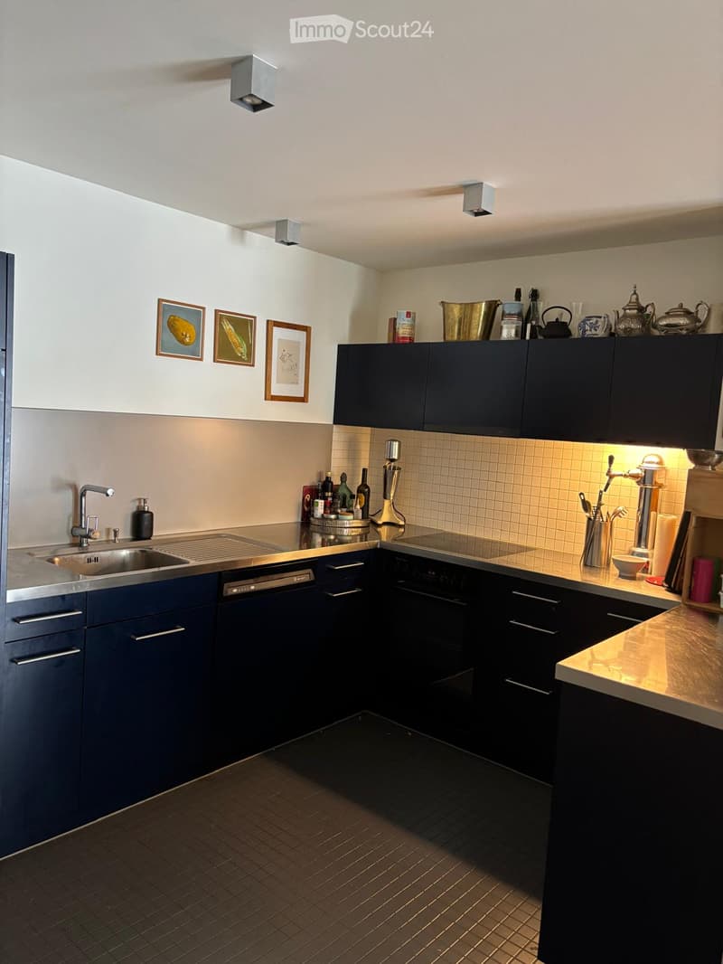 Modern kitchen with dark blue cabinets, stainless steel sink, dishwasher, and countertop. Features framed pictures on the wall and various kitchen items on the counter.
